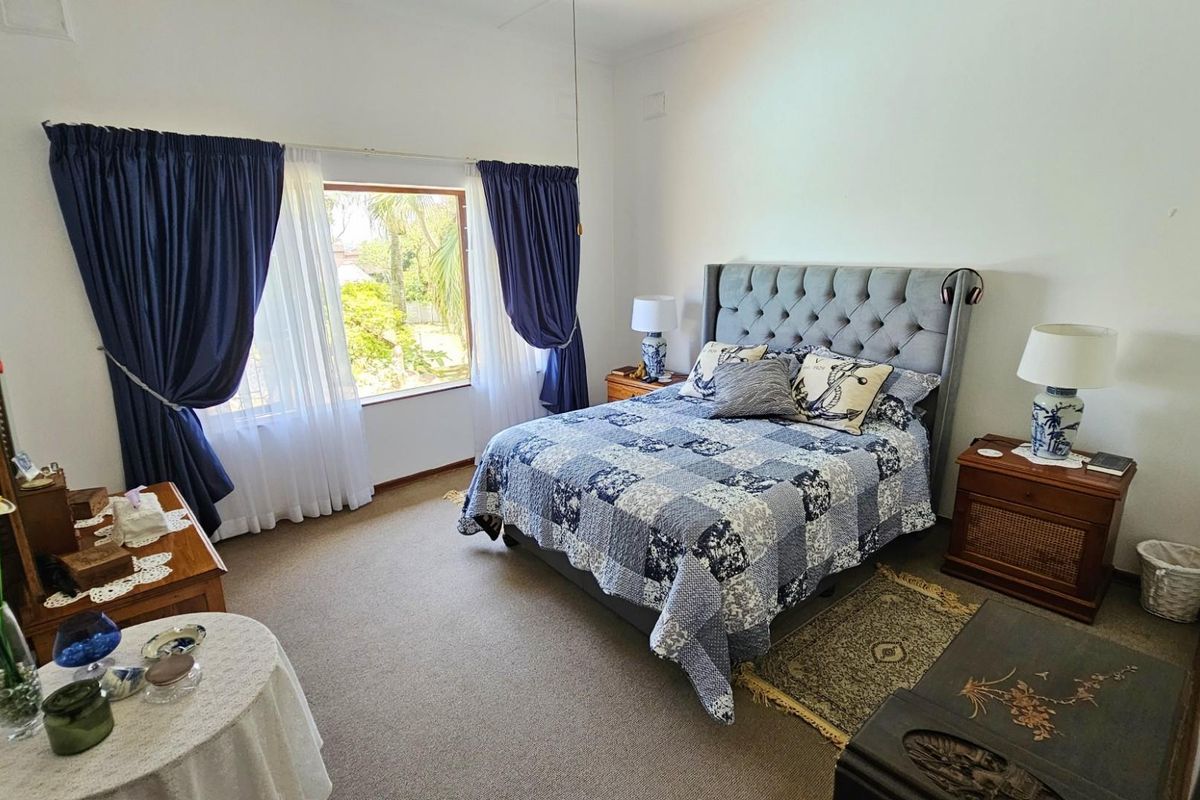 A well-lit bedroom featuring neutral carpeting, large windows with curtains, and ample space for a double bed and bedside tables.