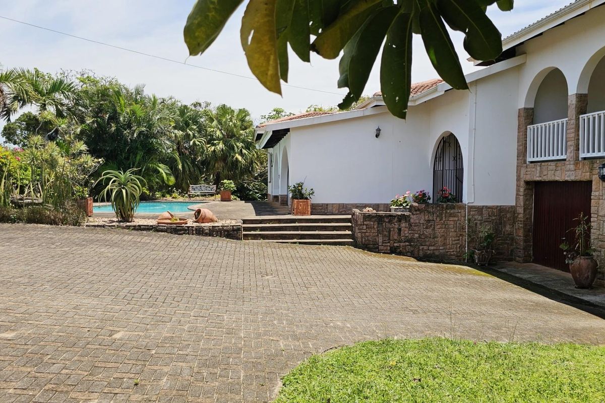 Spacious paved driveway leading to a residence with a swimming pool, landscaped garden, and covered patio area.