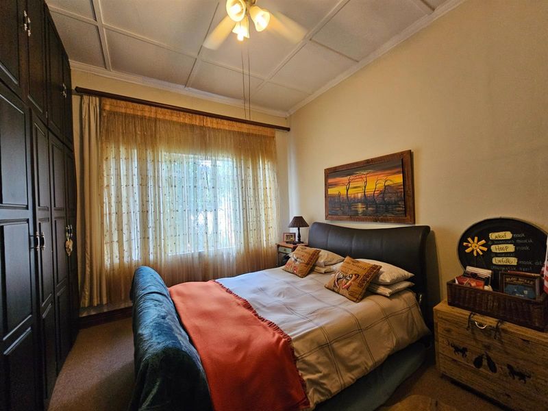 A cozy bedroom featuring built-in cupboards, a ceiling fan, and a tiled ceiling, providing a functional and comfortable living space.