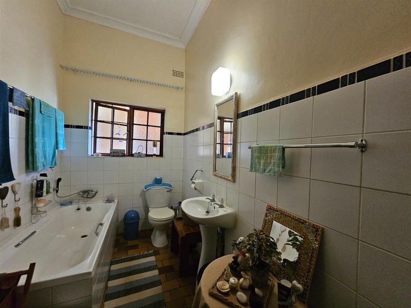 A functional bathroom featuring a bathtub, pedestal sink, toilet, and classic tiled wall finishes with a window for natural light.