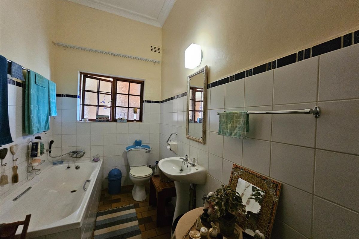 A functional bathroom featuring a bathtub, pedestal sink, toilet, and classic tiled wall finishes with a window for natural light.