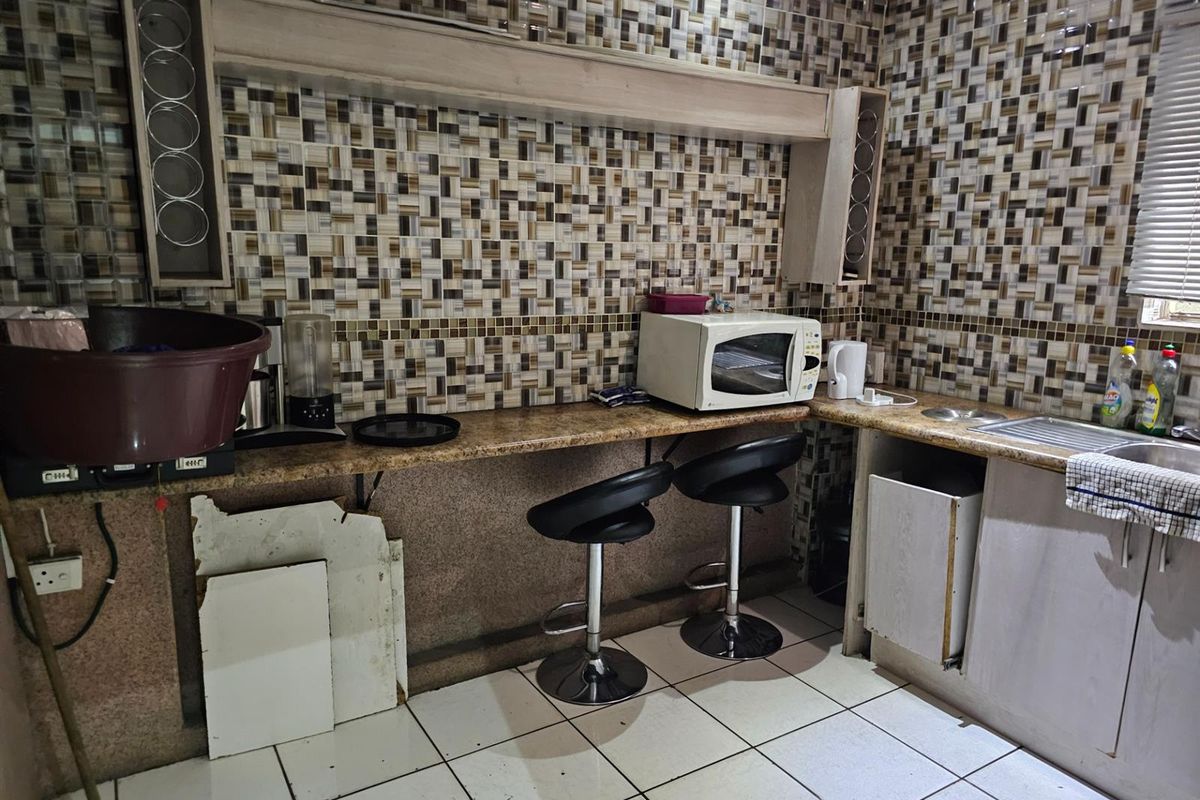 A dated kitchen area featuring mosaic wall tiles, a stone-look countertop, and integrated sink, currently showing signs of wear and missing cabinetry components.