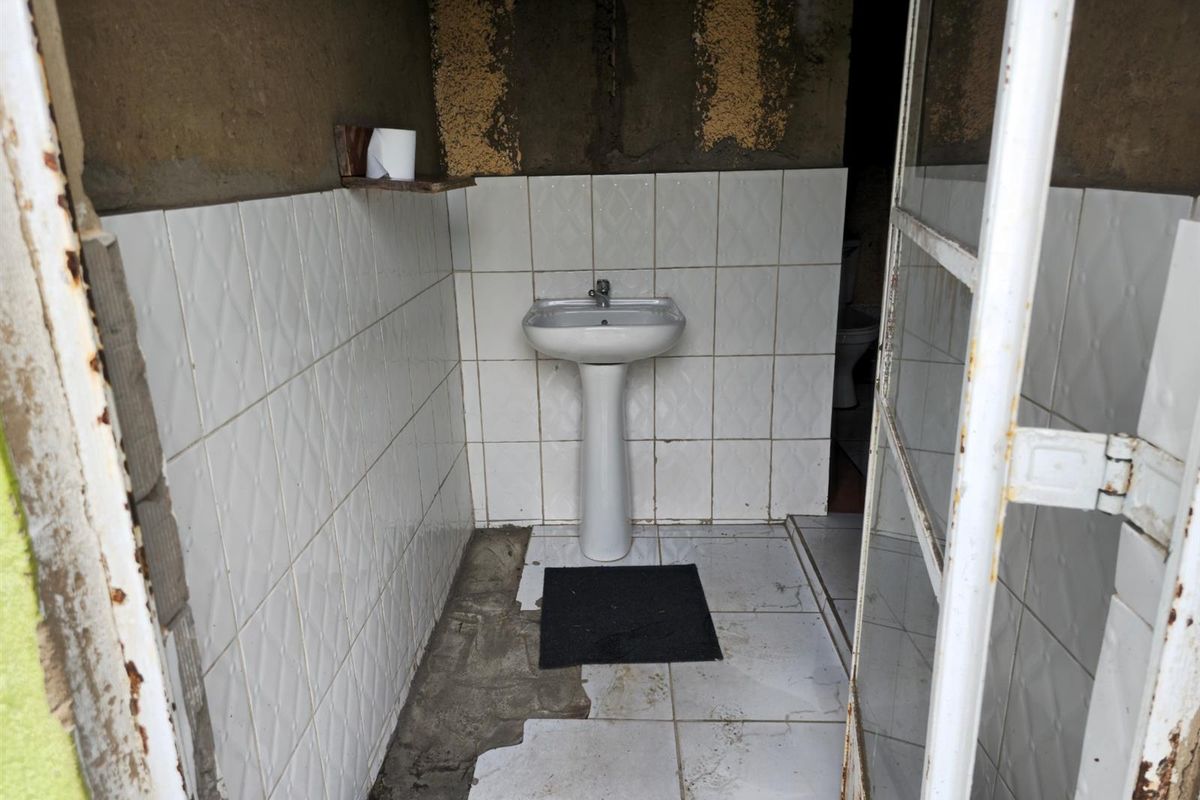 A small, unfinished bathroom featuring a pedestal basin and partial wall tiling, requiring significant renovation and repair to the flooring and wall finishes.