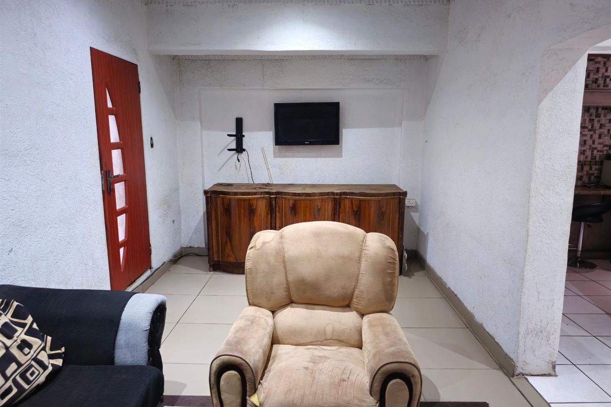 A living room area featuring tiled flooring, textured walls, and a built-in wall-mounted television setup.