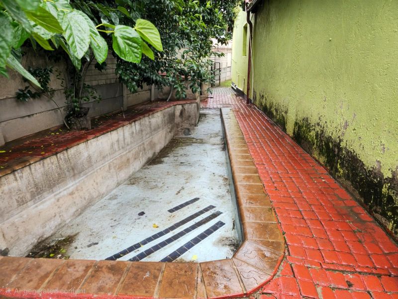An outdoor pool area featuring a paved walkway and a concrete pool basin, showing signs of significant wear and maintenance requirements.