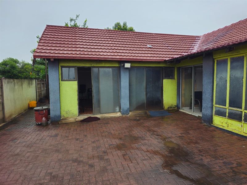 Rear exterior view of the property featuring a paved patio area, sliding glass doors, and a tiled roof structure.