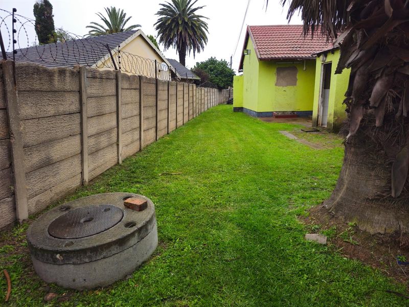A side garden area featuring a lawn, concrete boundary wall with security fencing, and a view of the rear building elevation.