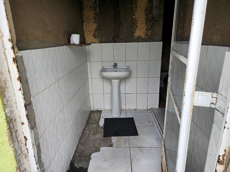 A small, unfinished bathroom featuring a pedestal basin and partial wall tiling, requiring significant renovation and repair to the flooring and wall finishes.