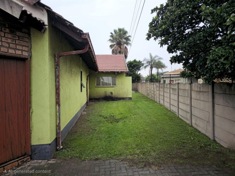 A view of the rear exterior of the property featuring a lawn, perimeter wall, and painted masonry walls with visible signs of wear.