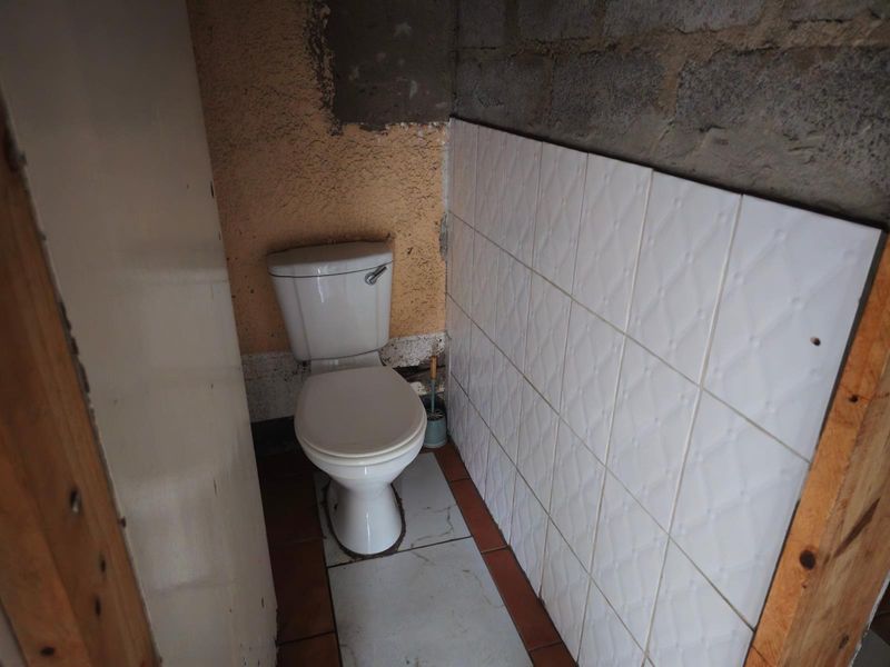 A small bathroom featuring a standard toilet, partially tiled walls, and unfinished exposed concrete blockwork, requiring significant renovation and finishing.