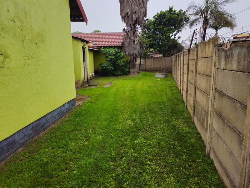 A side garden area featuring a lawn, enclosed by precast concrete walling with security wire, adjacent to the main house structure.