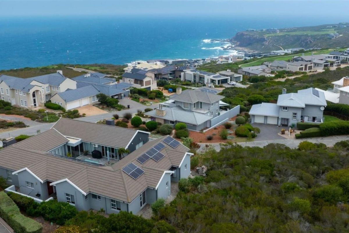 Aerial view of a coastal residential estate featuring modern homes with tiled roofs, solar panels, and proximity to the ocean.