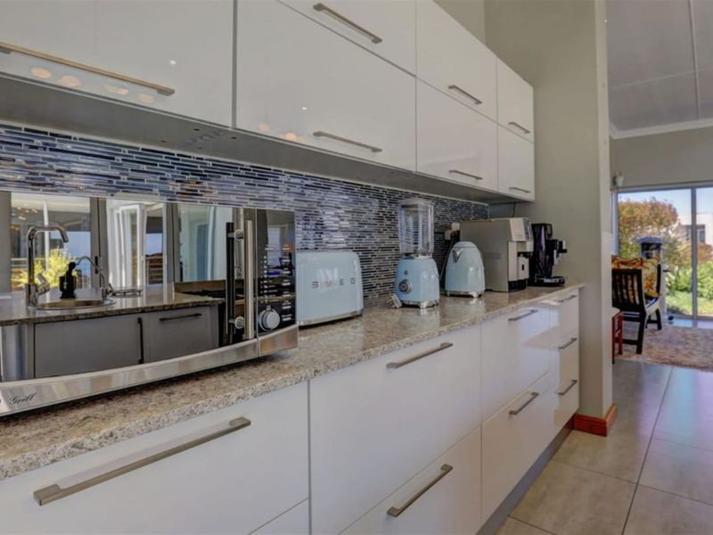 Modern kitchen featuring high-gloss white cabinetry, granite countertops, and a decorative mosaic tile backsplash, leading into an open-plan living area.