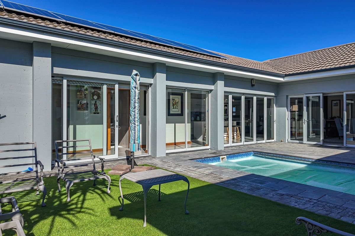 A well-maintained rear exterior featuring a swimming pool, paved surround, artificial lawn, and large sliding glass doors providing seamless indoor-outdoor flow.