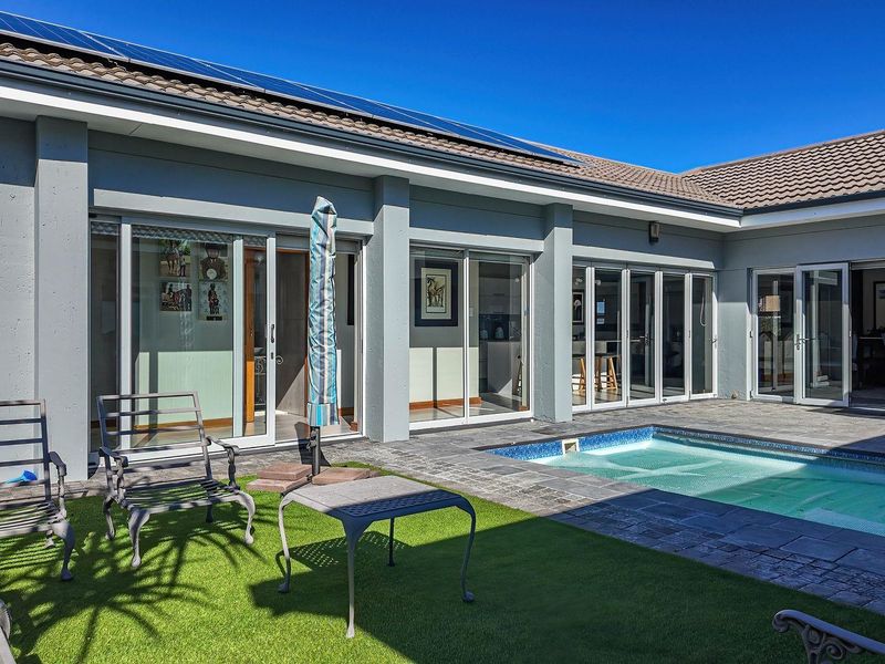 A well-maintained rear exterior featuring a swimming pool, paved surround, artificial lawn, and large sliding glass doors providing seamless indoor-outdoor flow.