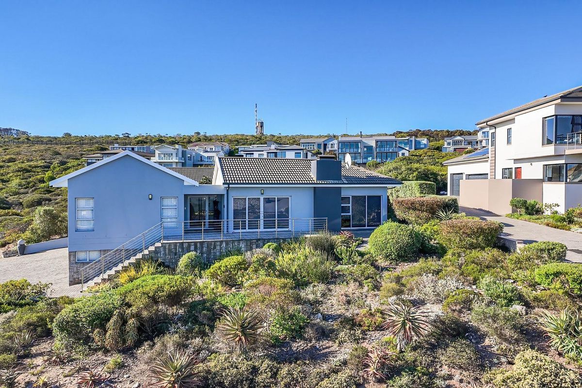 Elevated view of the rear exterior of the house, featuring a raised patio, landscaped garden, and paved driveway area.