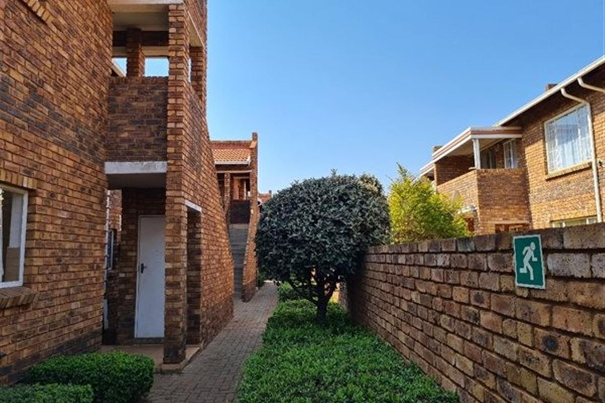 Exterior view of an apartment complex featuring face-brick architecture, paved walkways, and landscaped garden areas.