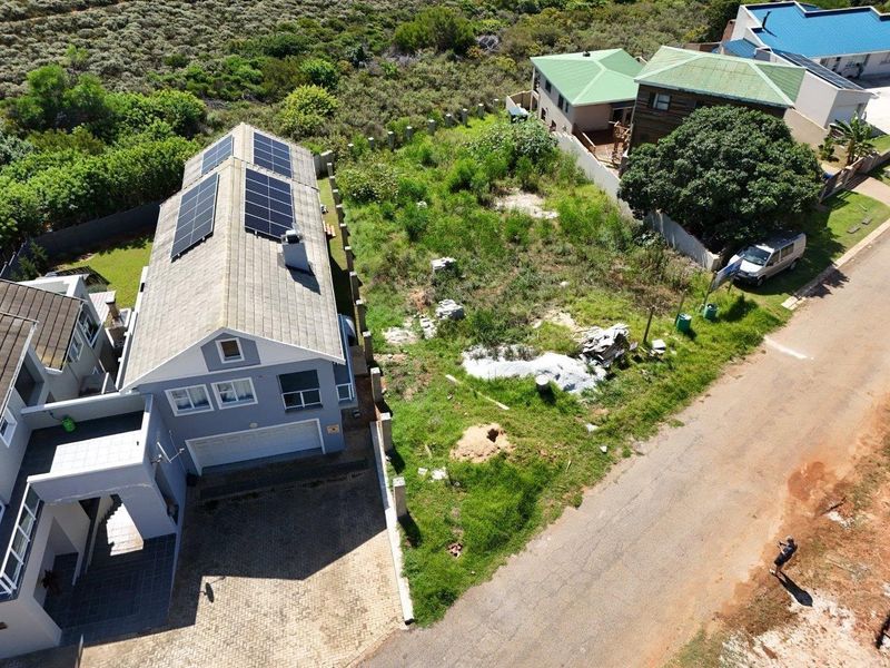 Aerial view of a residential property featuring a house with solar panels and an adjacent vacant plot with overgrown vegetation.