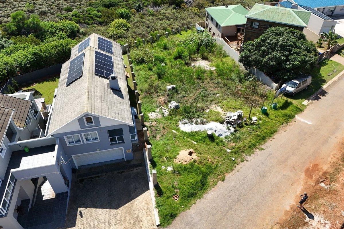 Aerial view of a residential property featuring a house with solar panels and an adjacent vacant plot with overgrown vegetation.