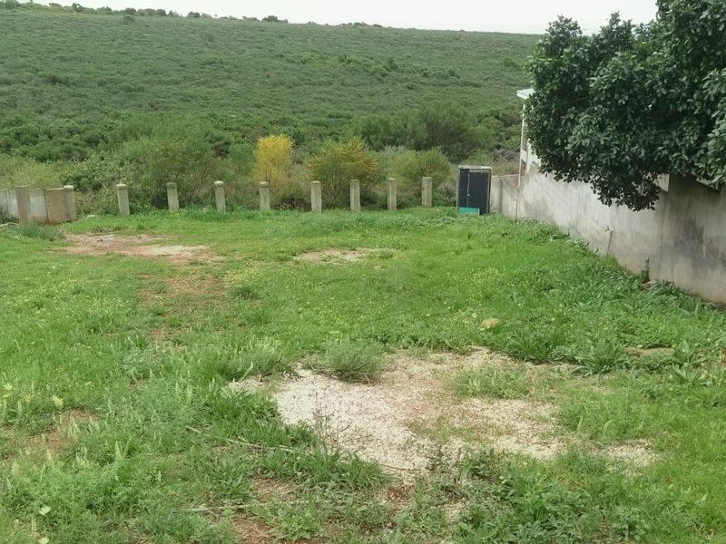 A vacant residential plot featuring a grass lawn, concrete boundary wall, and fence posts, overlooking a natural green landscape.