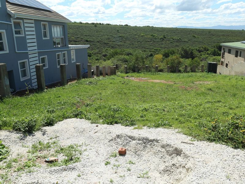 A view of the rear yard area featuring a sloped grass plot, gravel patch, and concrete retaining posts adjacent to the neighboring residential structure.