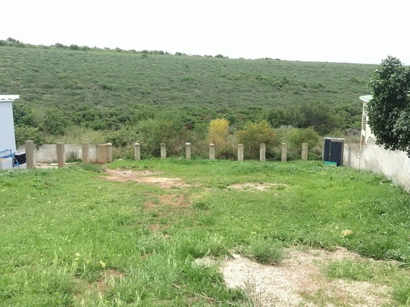 A view of the rear yard area featuring a grass lawn, perimeter boundary posts, and a concrete wall, overlooking natural landscape.