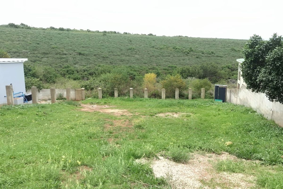 A view of the rear yard area featuring a grass lawn, perimeter boundary posts, and a concrete wall, overlooking natural landscape.