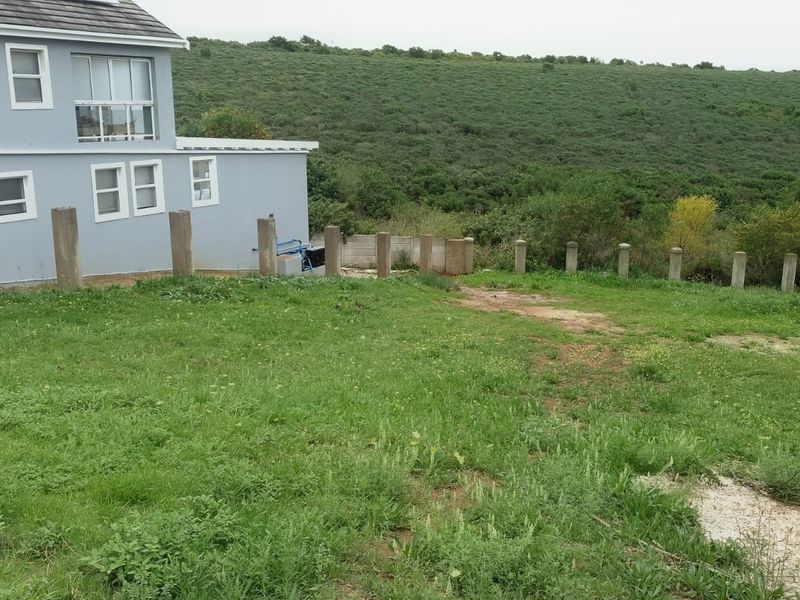 Rear view of the residential property showing a grass lawn, concrete fence posts, and surrounding natural landscape.