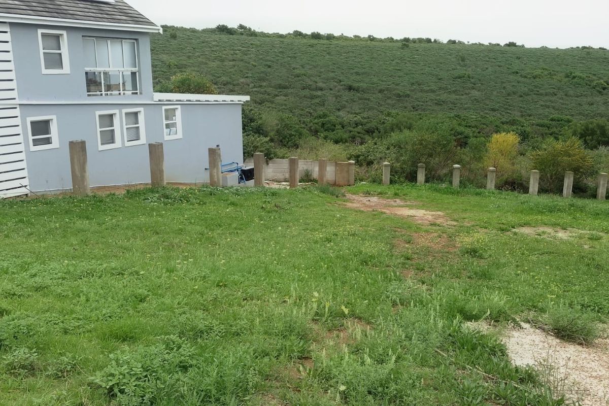 Rear view of the residential property showing a grass lawn, concrete fence posts, and surrounding natural landscape.