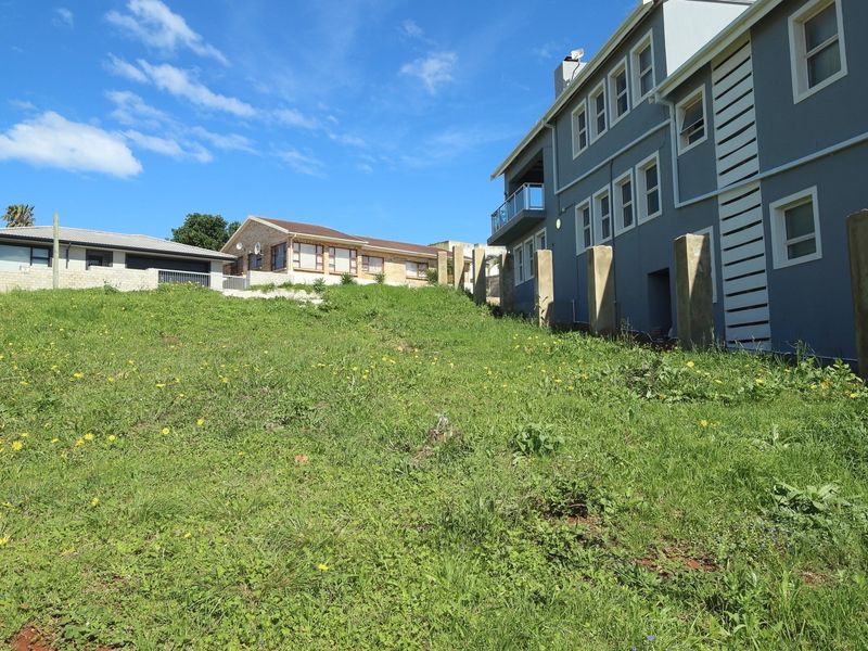 A view of the sloped vacant residential land with existing concrete boundary posts, adjacent to a multi-story residential building.
