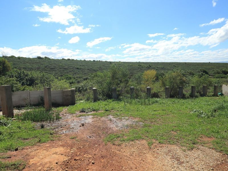 A view of the rear vacant land area featuring a concrete boundary fence and natural landscape surroundings.
