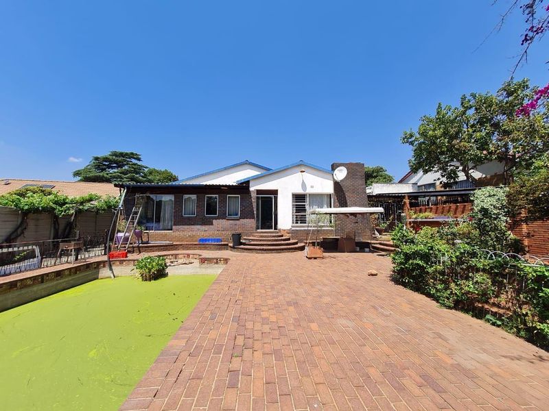 Rear exterior view of the house featuring a brick-paved patio area and a swimming pool requiring maintenance.