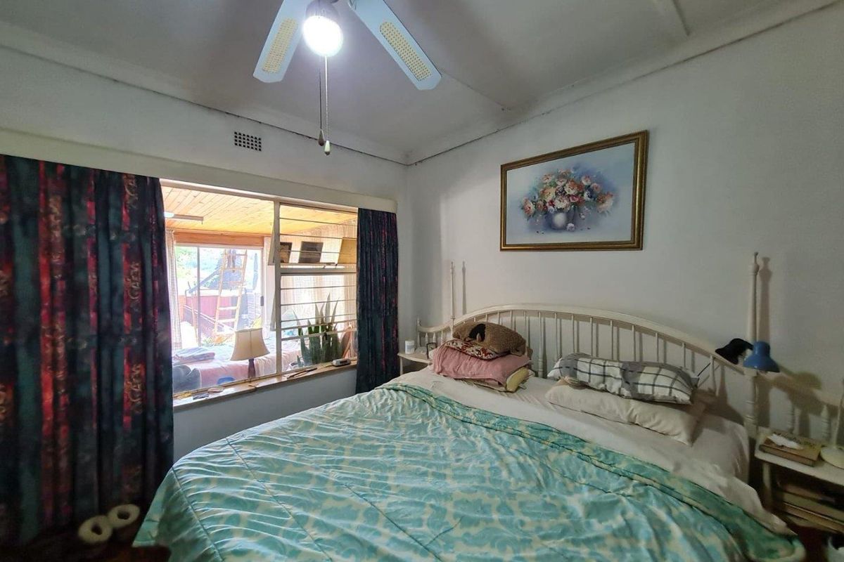 A bedroom featuring a ceiling fan and a large window with security bars, overlooking an adjacent patio area.
