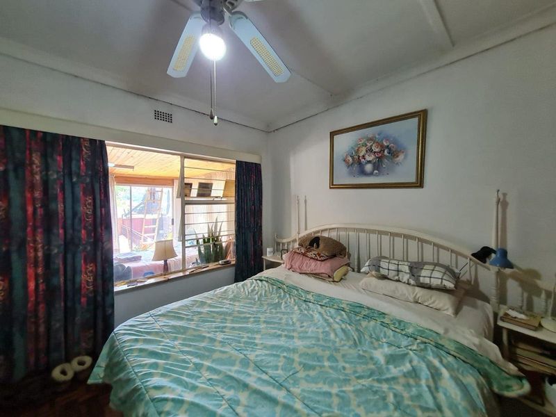 A bedroom featuring a ceiling fan and a large window with security bars, overlooking an adjacent patio area.