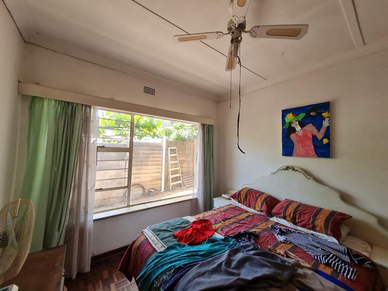 A bedroom featuring parquet flooring, a large steel-framed window, and a ceiling fan requiring repair.