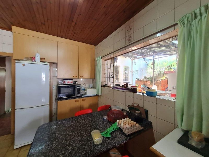 A dated kitchen featuring timber ceilings, granite countertops, and a pass-through window, showing signs of moisture damage on the tiled wall.