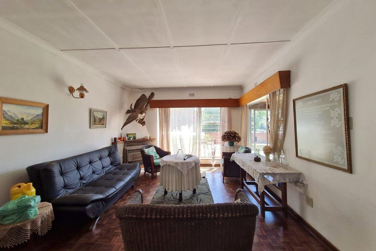 A spacious living room featuring classic parquet flooring and large sliding glass doors that provide ample natural light and access to the exterior.