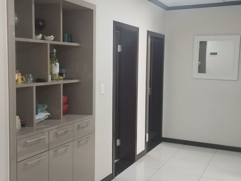 A clean hallway featuring neutral wall tones, white tiled flooring, and built-in storage cabinetry with dark door frames.