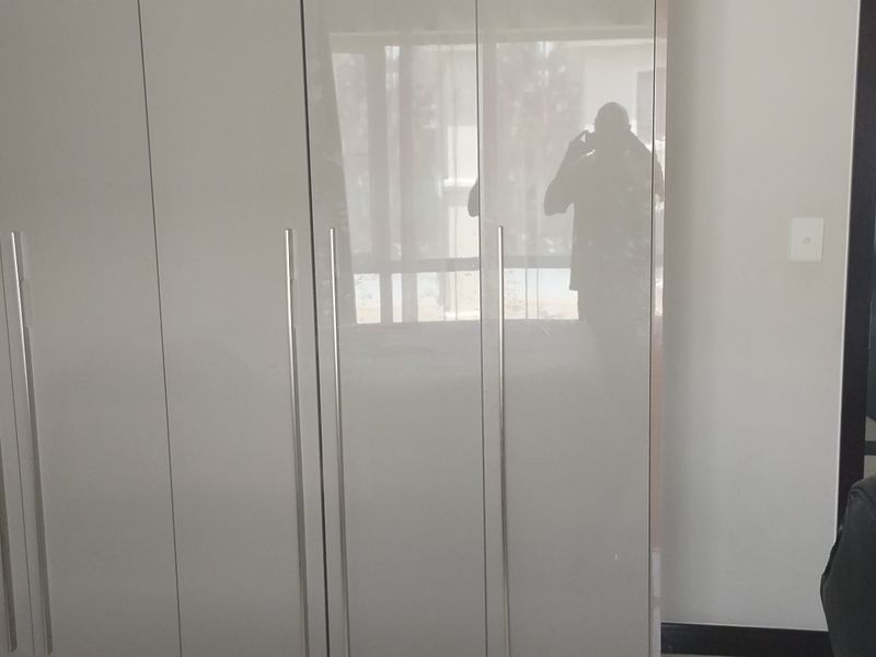 A bedroom featuring modern high-gloss built-in cupboards and tiled flooring, with a view into an adjacent room.