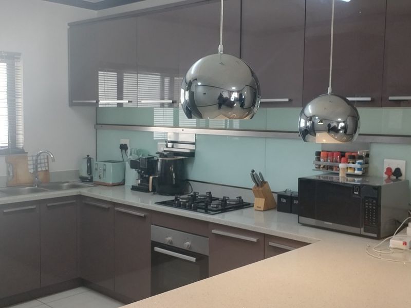 Modern kitchen featuring high-gloss cabinetry, stone countertops, a gas hob, built-in oven, and a sleek glass splashback with contemporary pendant lighting.