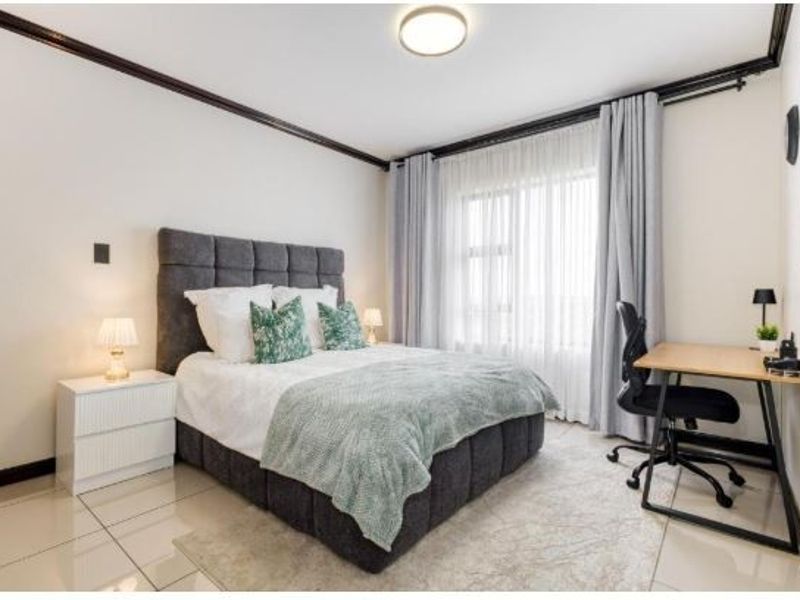 A well-maintained bedroom featuring tiled flooring, neutral walls with dark crown molding, and large windows with curtain tracks.