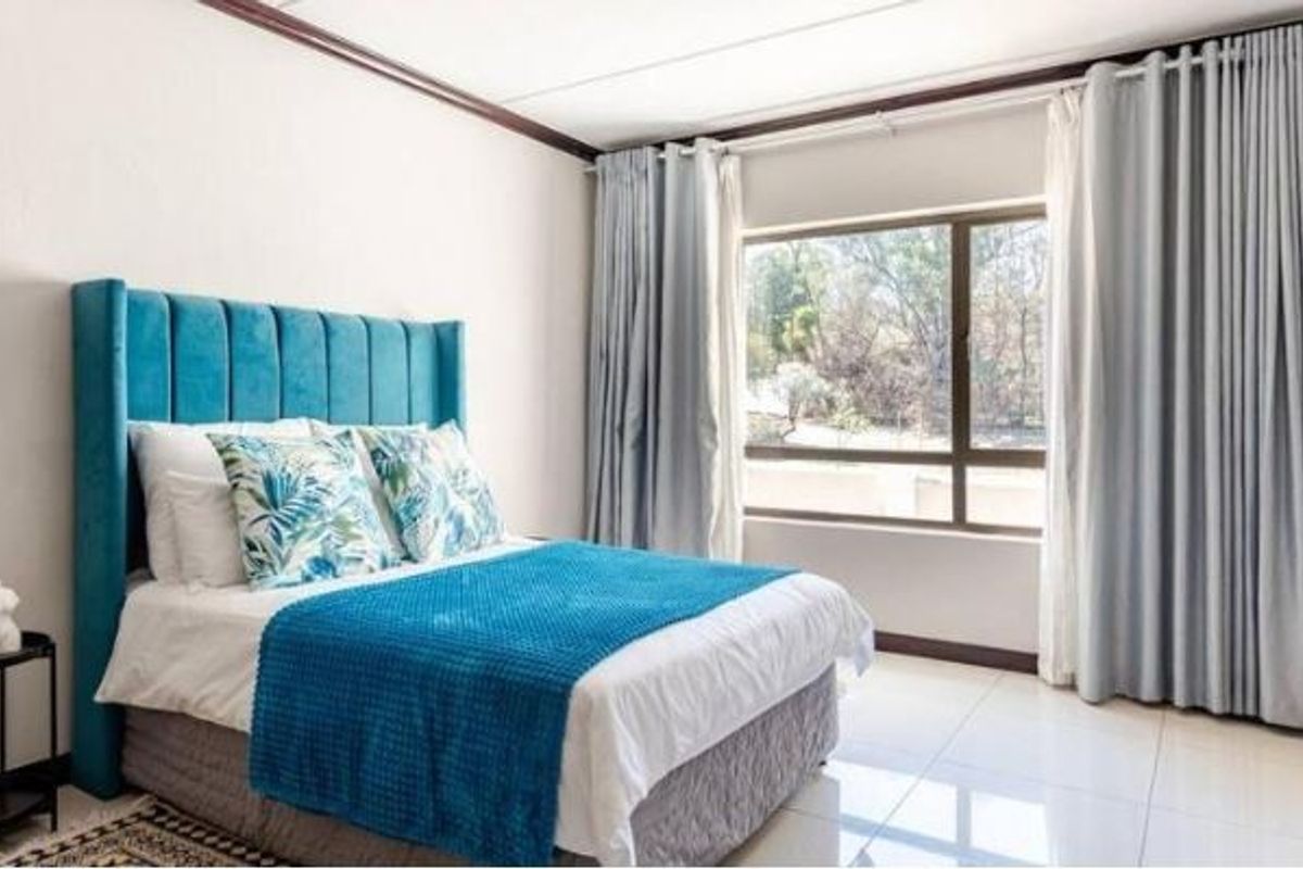 A bright and well-maintained bedroom featuring large windows with floor-to-ceiling curtains and neutral tiled flooring.