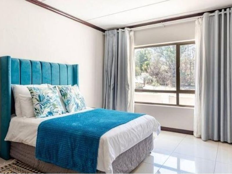A bright and well-maintained bedroom featuring large windows with floor-to-ceiling curtains and neutral tiled flooring.