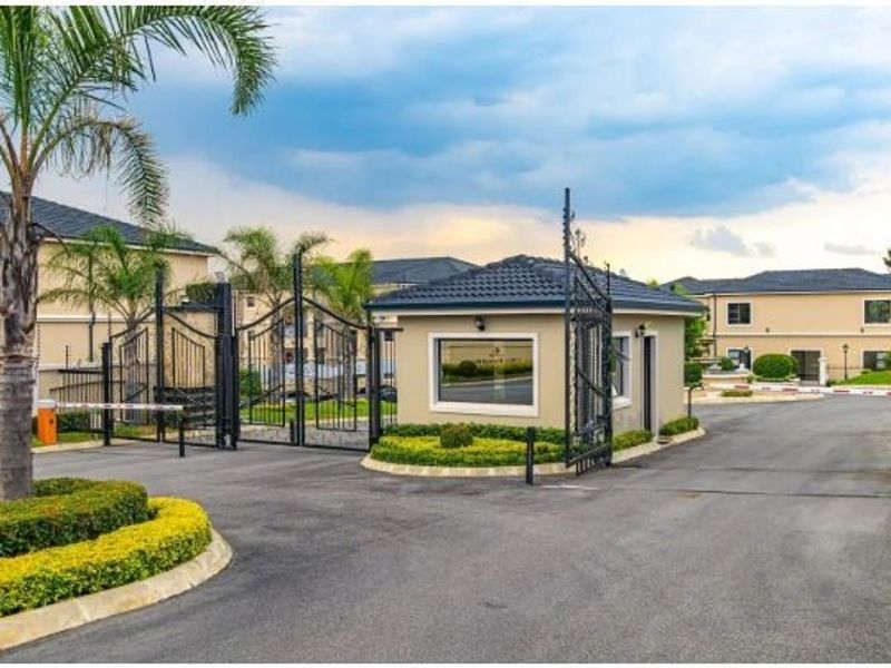 The secure entrance to the townhouse complex features a manned guard house, automated gates, and well-maintained paved access roads with landscaped surroundings.