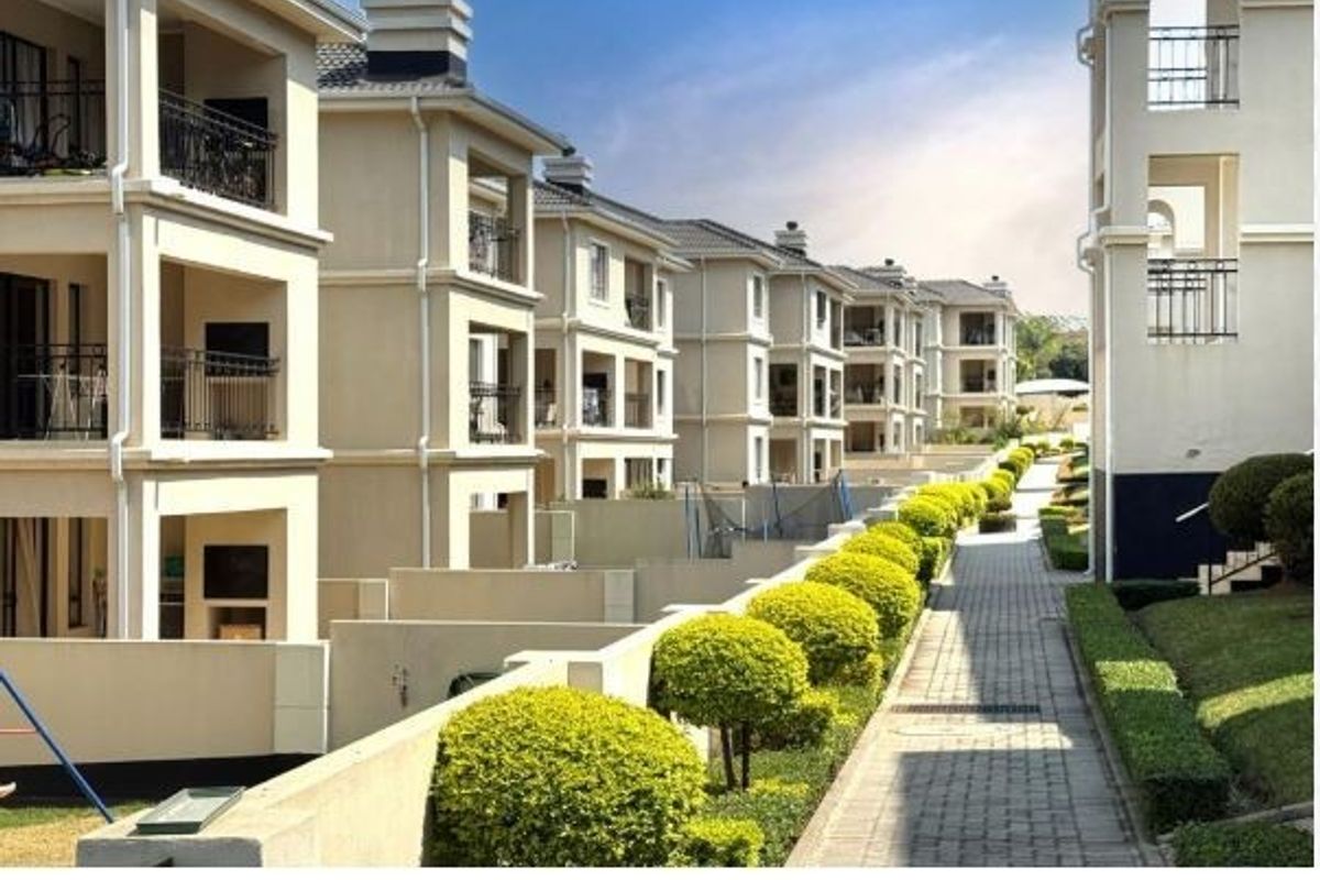 A view of the townhouse complex exterior featuring paved walkways, landscaped hedges, and multi-level balconies with metal railings.