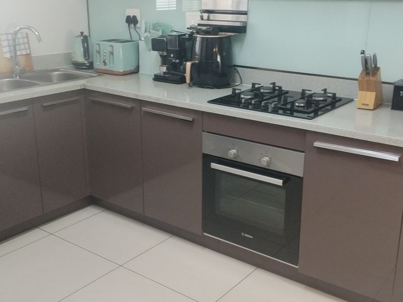 Modern kitchen featuring sleek brown cabinetry, stone countertops, a gas hob, built-in oven, and a glass splashback with tiled flooring.
