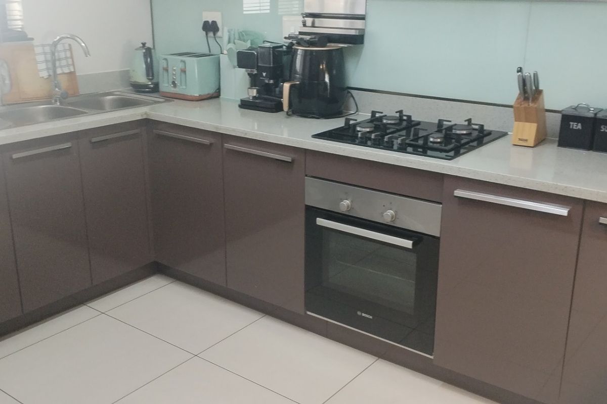 Modern kitchen featuring sleek brown cabinetry, stone countertops, a gas hob, built-in oven, and a glass splashback with tiled flooring.