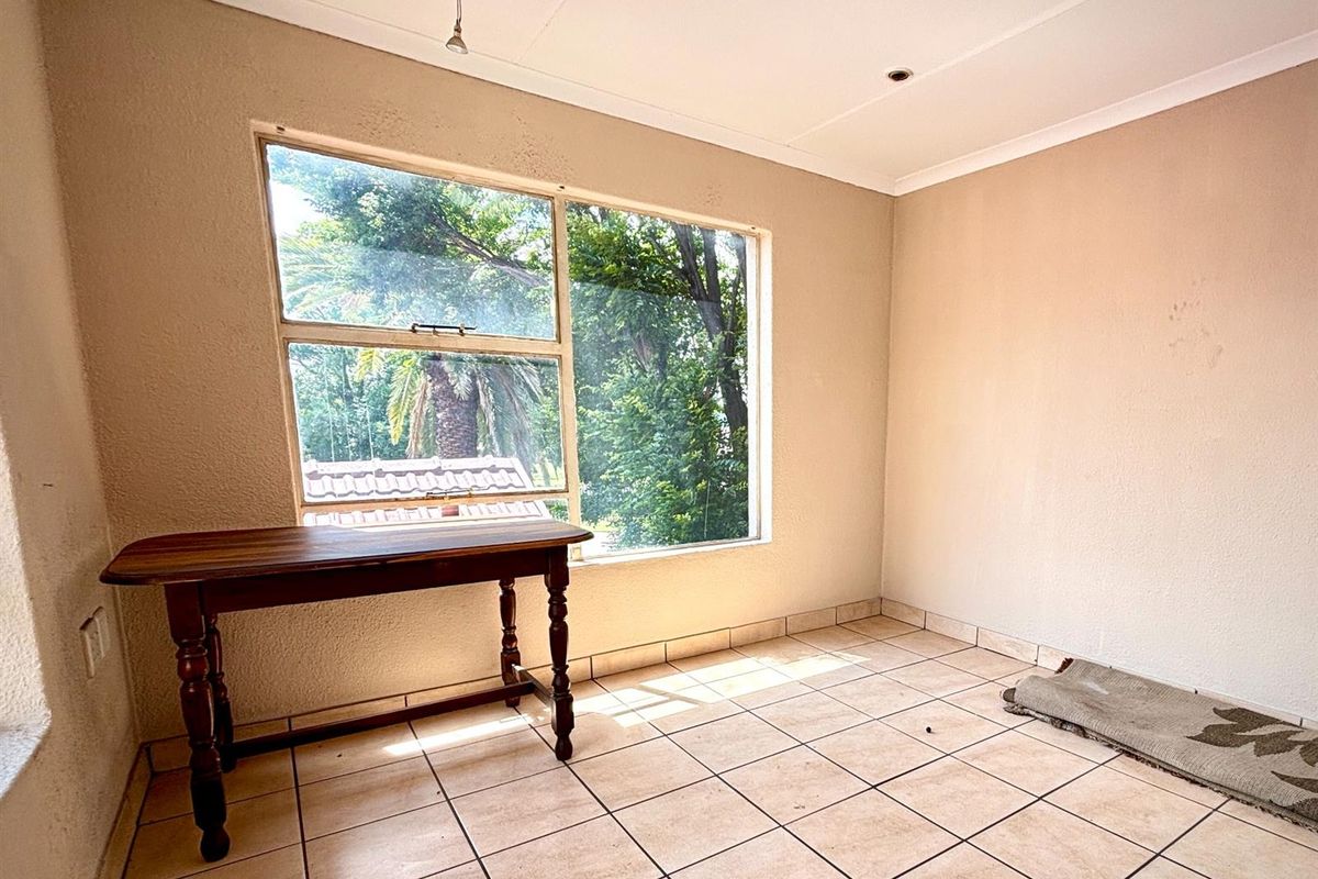A bright, empty room featuring neutral tiled flooring and a large window providing natural light and garden views.