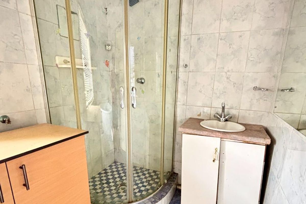 A dated bathroom featuring a corner shower enclosure, a small vanity unit with a basin, and blue floor tiling.