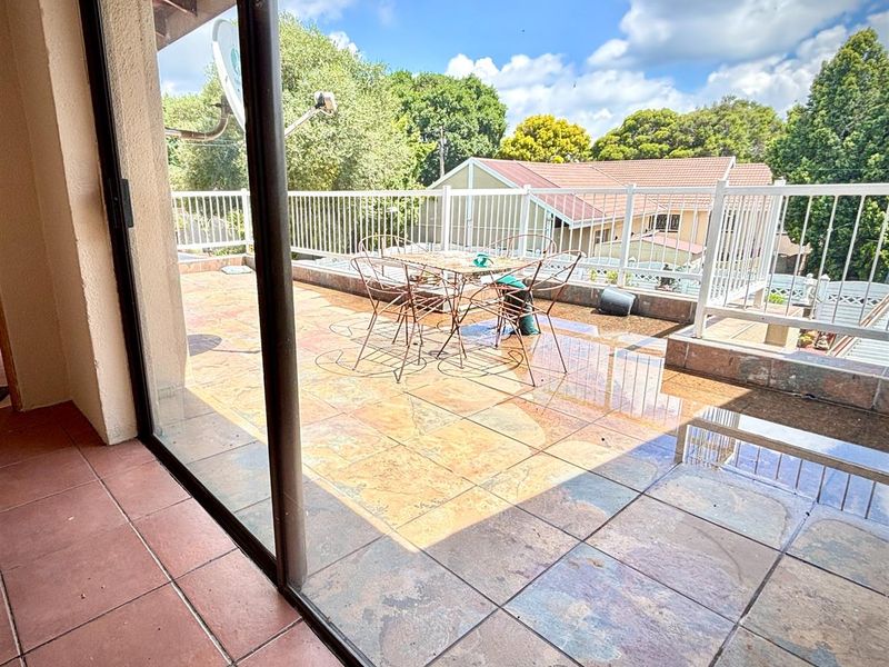 Spacious outdoor balcony featuring tiled flooring and white metal railings, offering an open-air space accessible through large sliding glass doors.